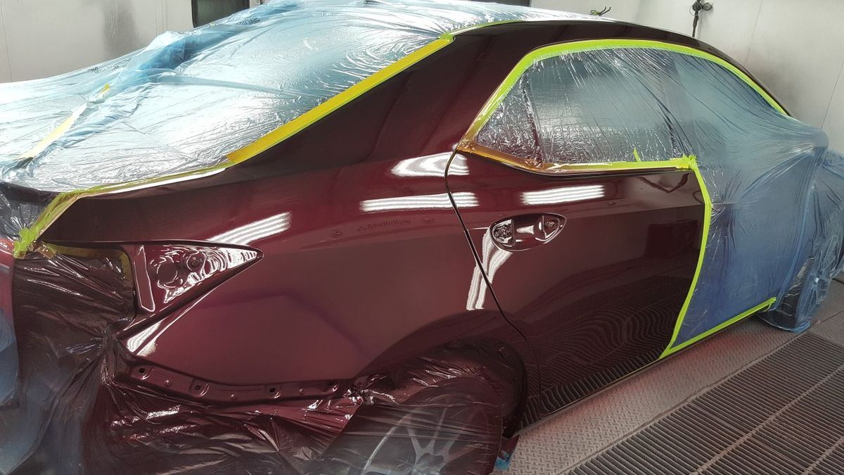 Maroon sedan masked and taped, prepped for paint in the booth